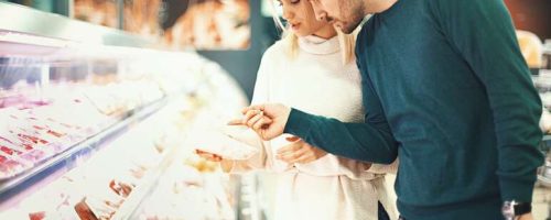 Closeup side view of a late 20's couple choosing some fresh meat for tonight's dinner. They are reading label on one of the packages and seem a bit uncertain about it.