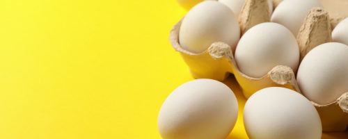Egg box with fresh eggs on yellow background