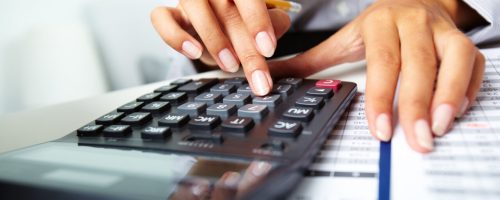 Photo of hands holding pencil and pressing calculator buttons over documents
